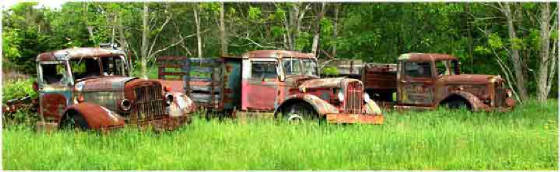 3 Autocar trucks rusting in a field